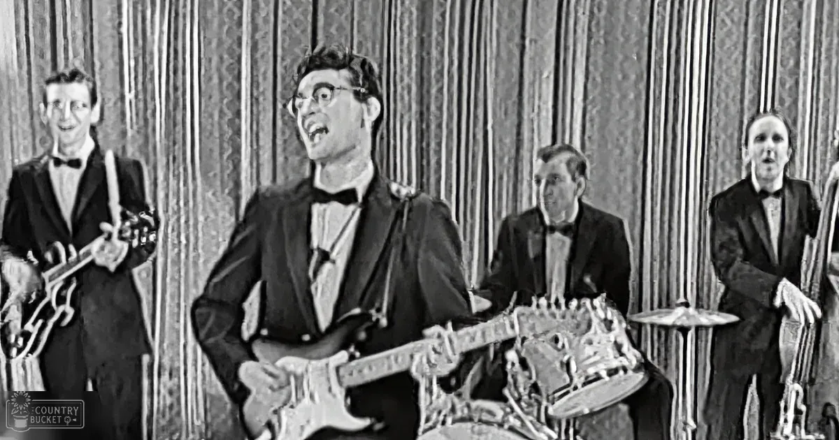 A man in a suit plays guitar while a band performs in a vintage setting.