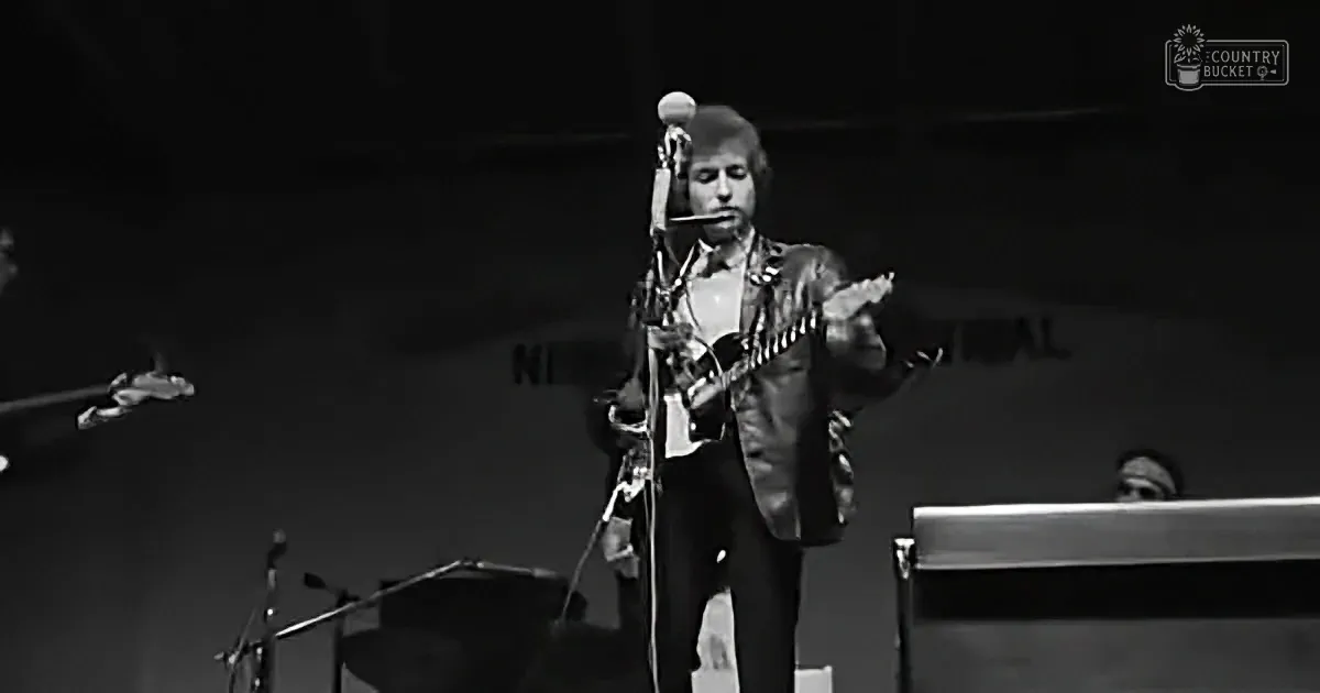 A man in a suit plays a guitar on stage, with a microphone and other instruments visible.