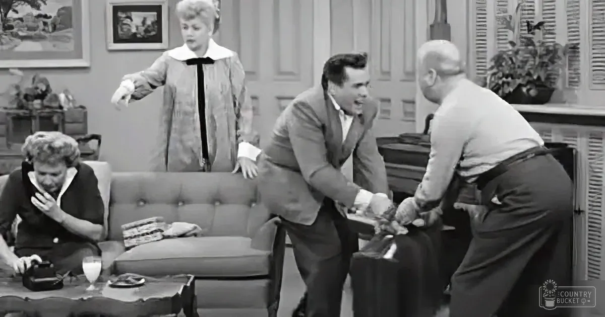 A man in a suit shakes hands with another, while a woman in a dress and another woman sit in the background.