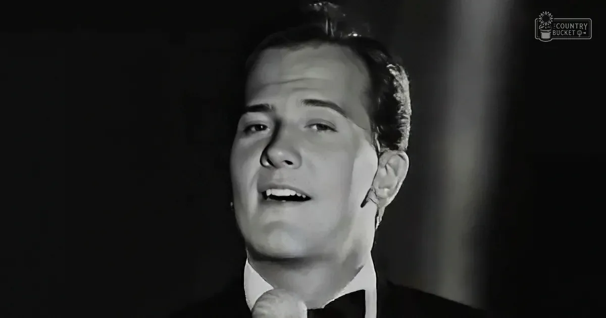 A man in a suit sings into a microphone, his mouth open, in a black-and-white image.