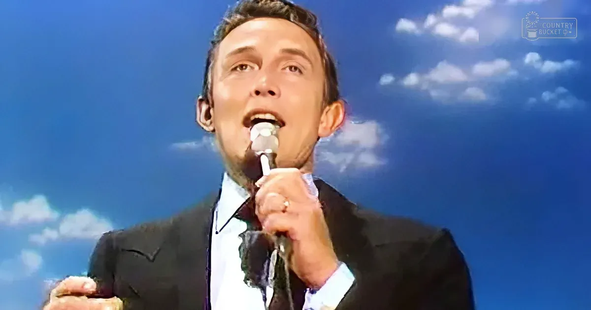 A man in a suit sings into a microphone against a blue sky backdrop.