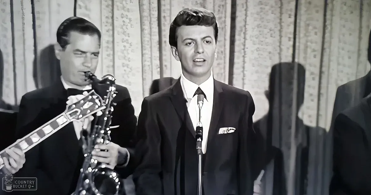 A man in a suit sings into a microphone while another plays a saxophone in the background.