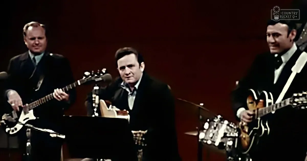 A man in a suit sings on stage with two guitarists, one playing a Les Paul.