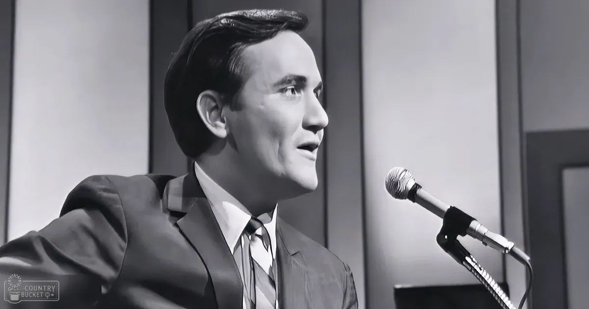 A man in a suit and tie is speaking into a microphone, looking to the side.