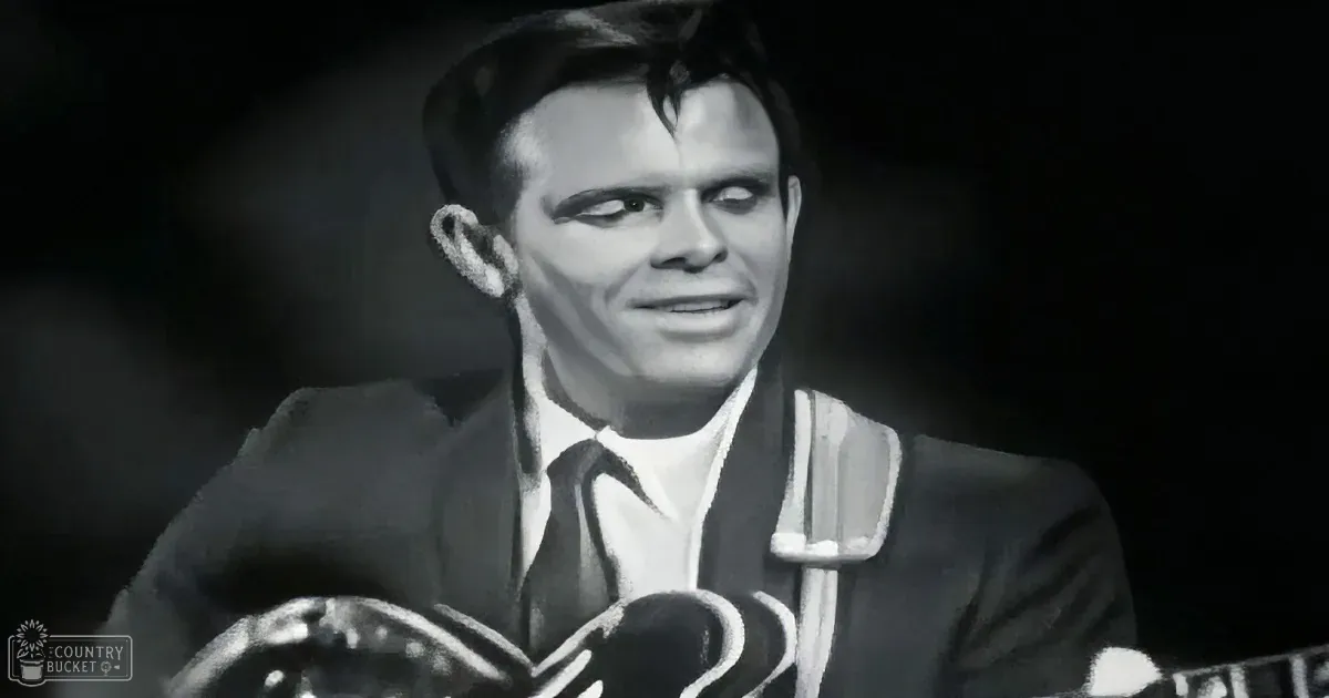 A man in a suit and tie is speaking into a microphone, with a dark background.
