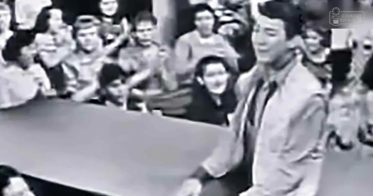 A man in a suit and tie is standing in front of a crowd, possibly giving a speech or presentation.