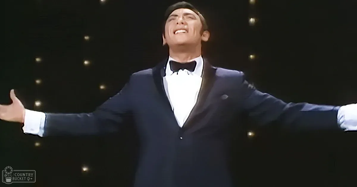 A man in a tuxedo with arms outstretched, smiling, and wearing a bow tie.
