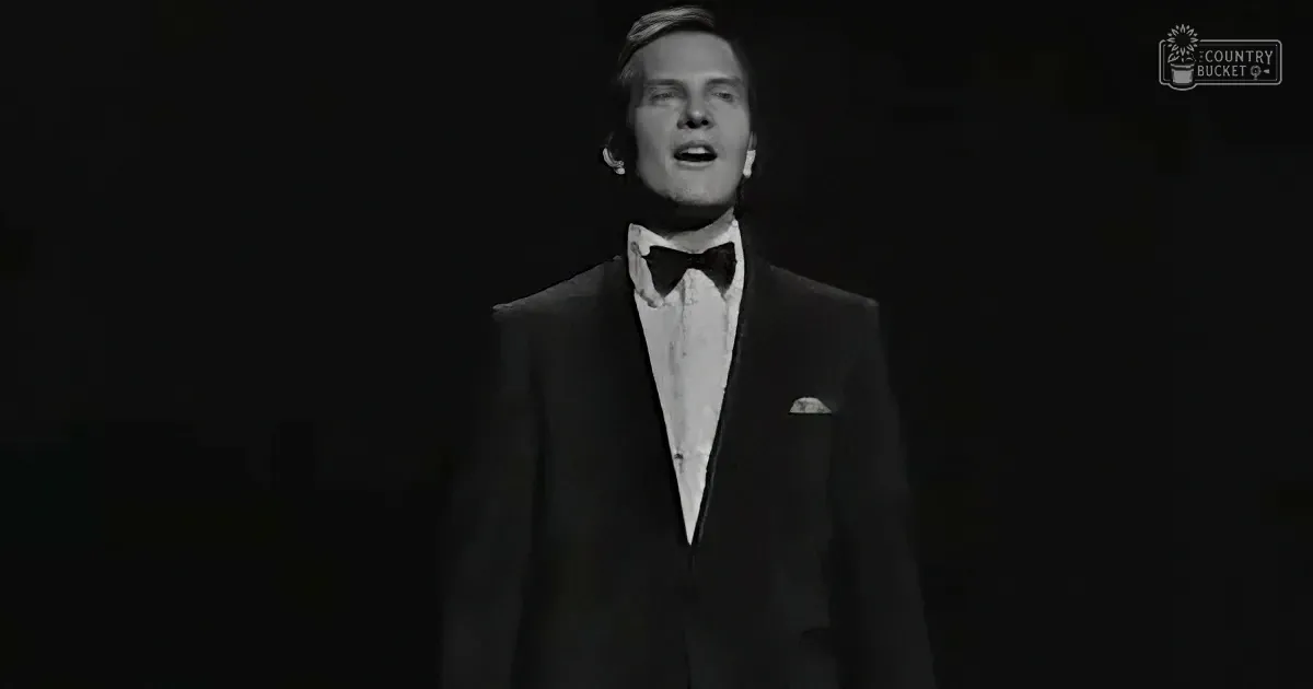 A man in a tuxedo sings against a dark background.