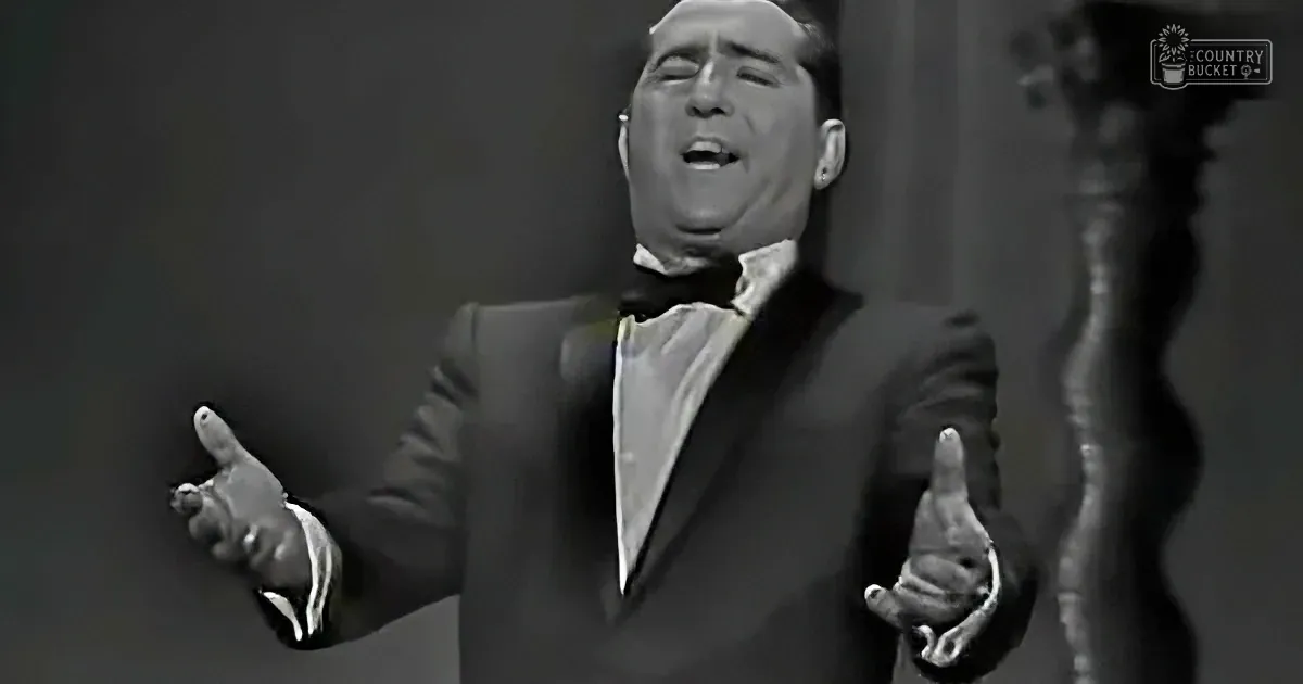A man in a tuxedo sings passionately with outstretched arms, captured in a black-and-white image.