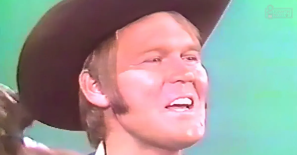 An adult male in a formal white shirt and dark cowboy hat against a solid green background, suggesting an indoor setting with even lighting.