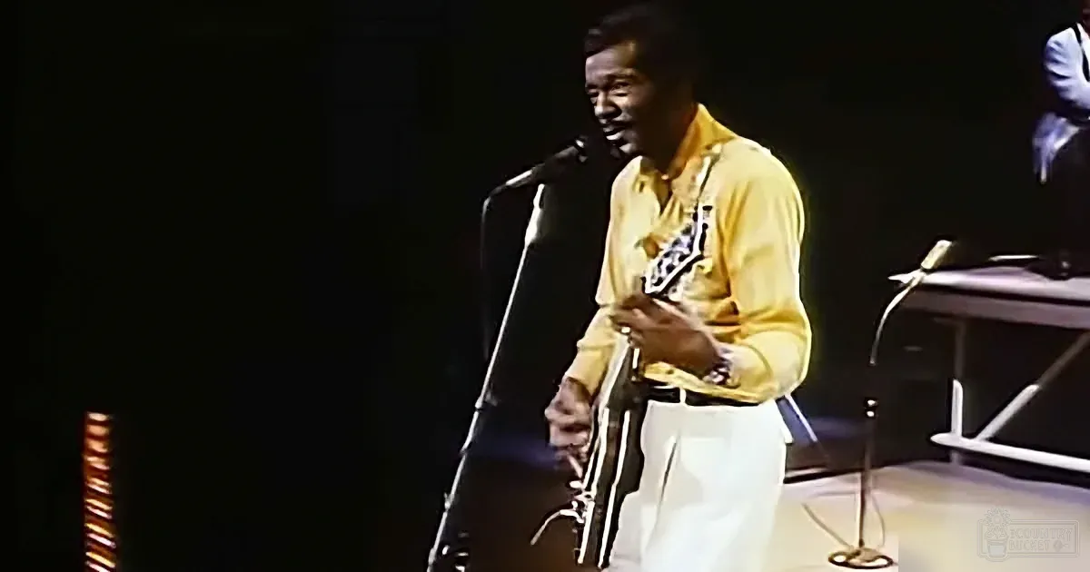A man in a yellow shirt plays a saxophone on stage with a microphone in front of him.