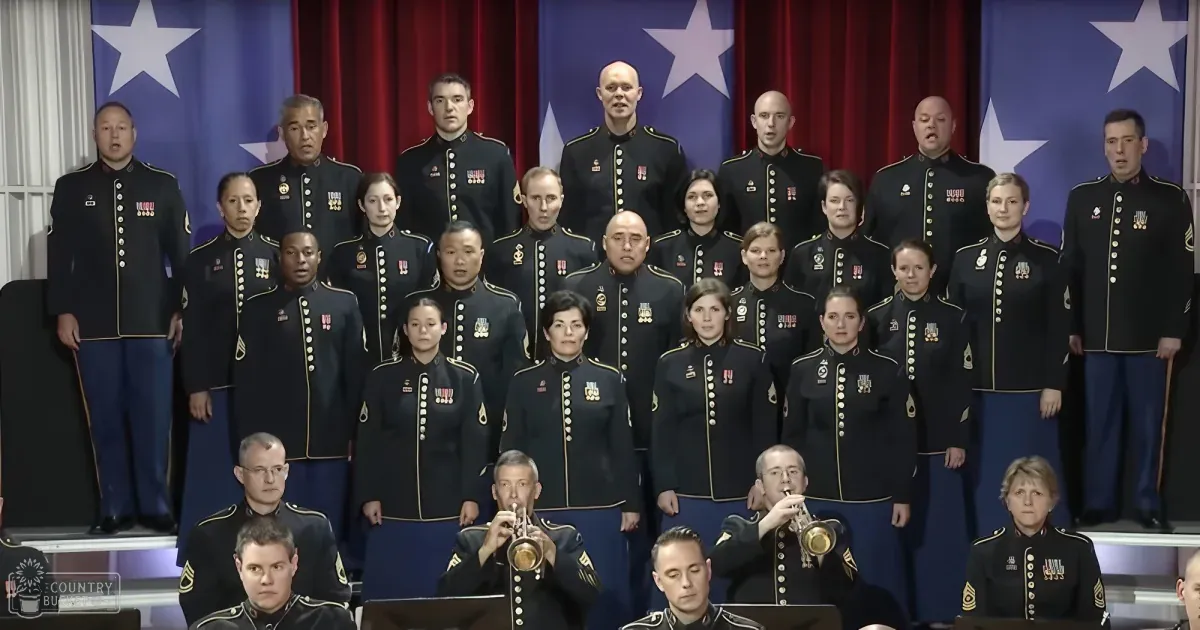 A military choir in uniform stands in formation, with a red curtain and stars in the background.