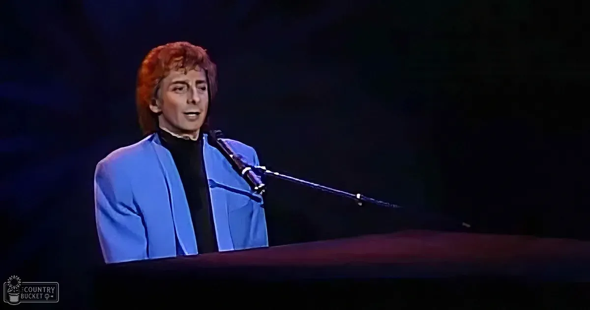 A person in a blue suit sings into a microphone on stage, with a dark background.