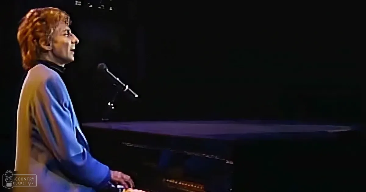 A person with red hair plays piano on stage, illuminated by stage lights.