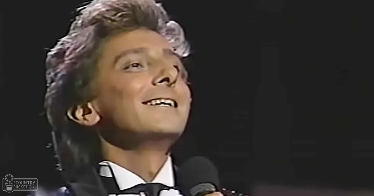 A person with short, curly hair and a white shirt smiles while holding a microphone.