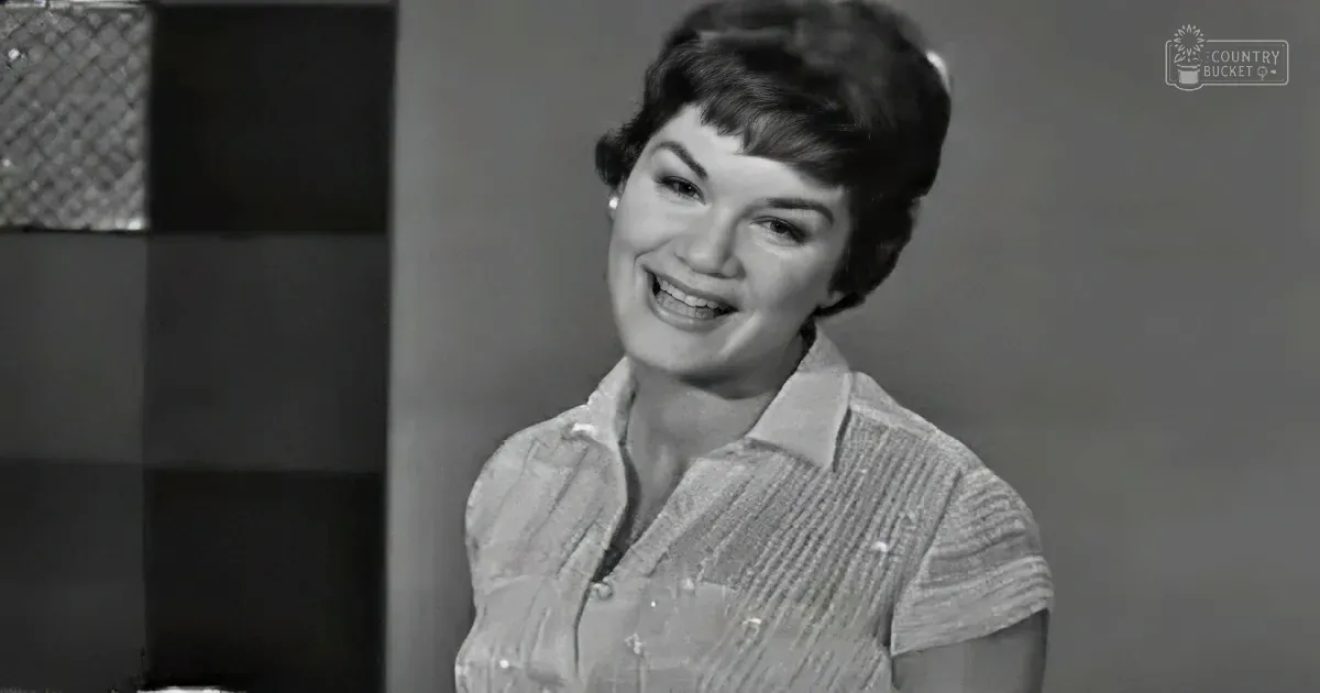 A smiling woman in a striped shirt, likely from a vintage TV show, with a blurred background.