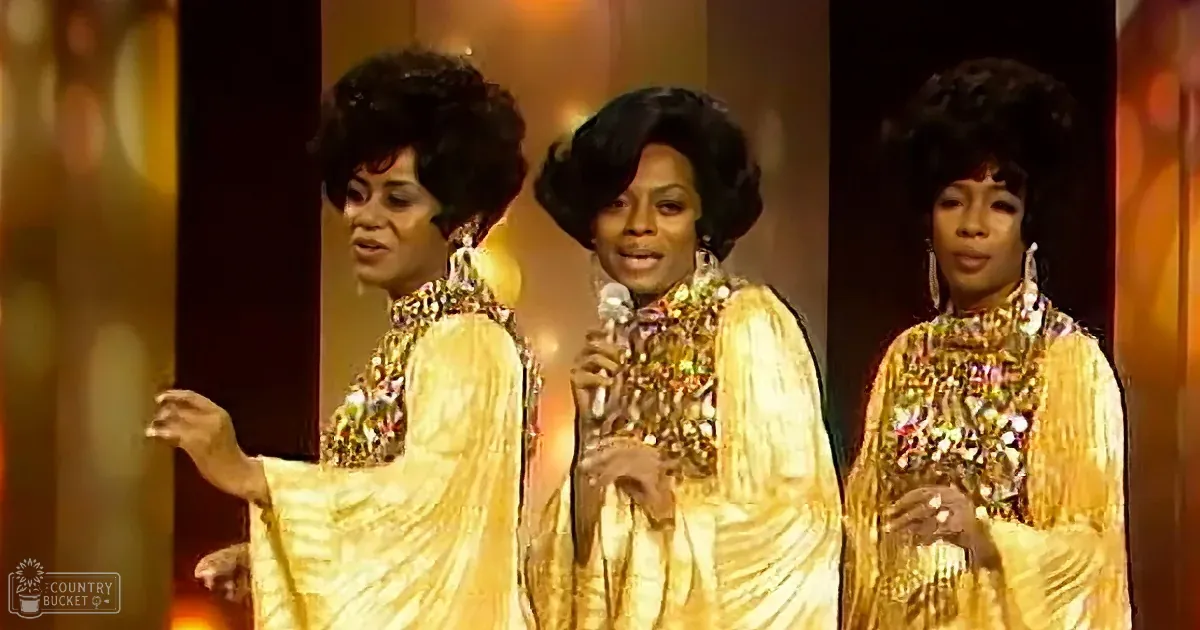 Three women in gold sequined gowns with afro hairstyles perform on stage.