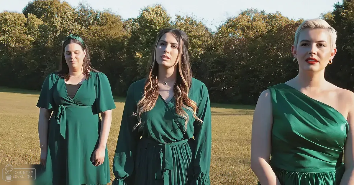 Three women in green dresses stand in a field with trees in the background.