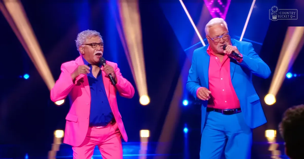 Two men in bright suits sing on stage with colorful lights behind them.