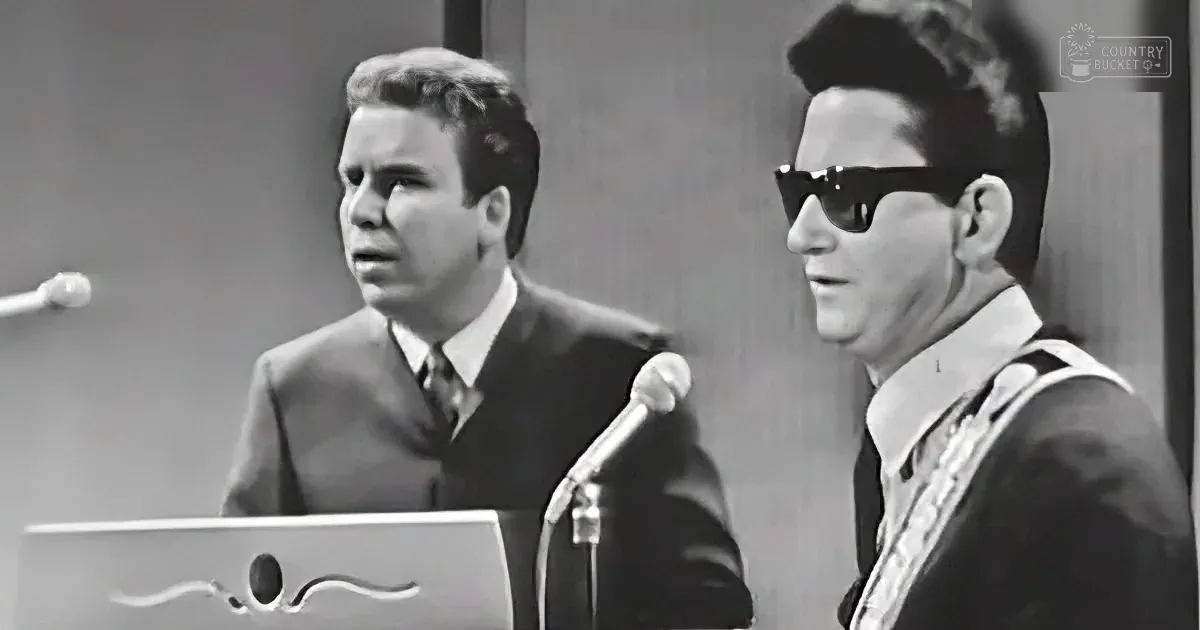Two men, one in sunglasses, are performing or speaking at a podium with microphones.