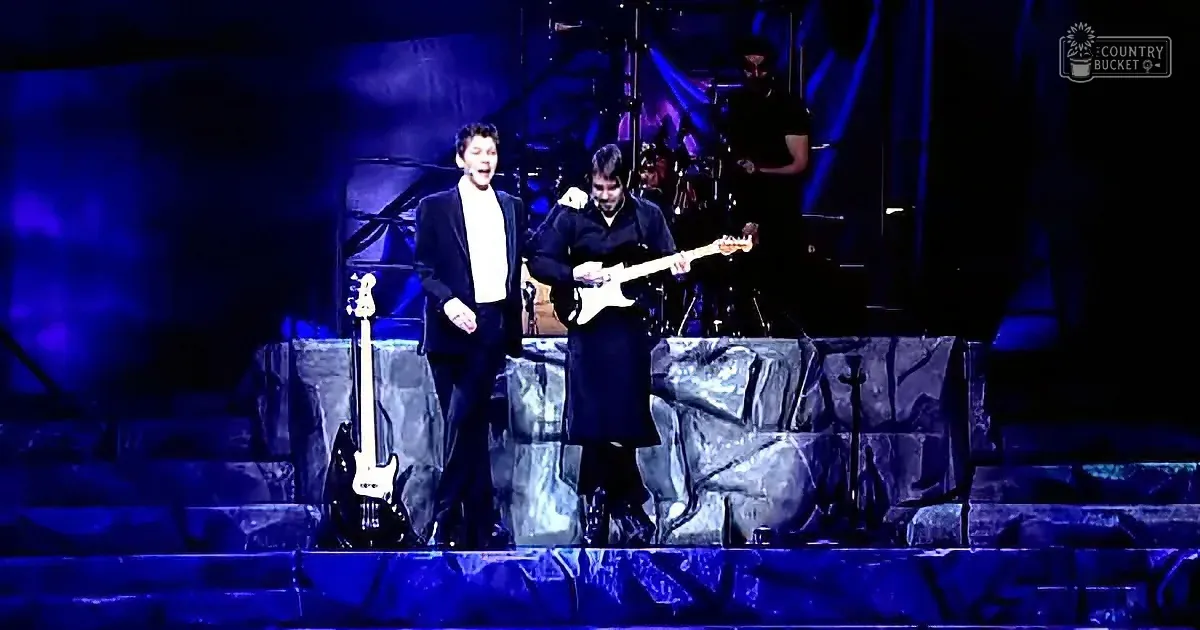 Two musicians perform on stage, one singing, the other playing guitar, under blue lighting.