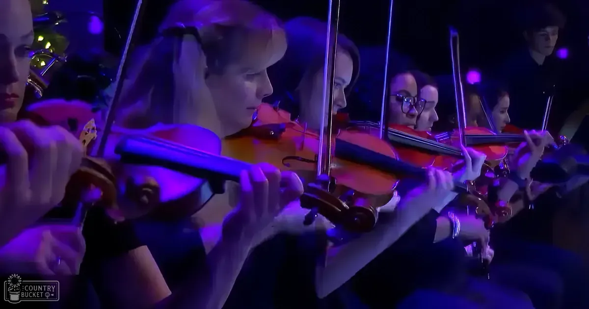 Violinists in a row, playing under purple stage lighting.