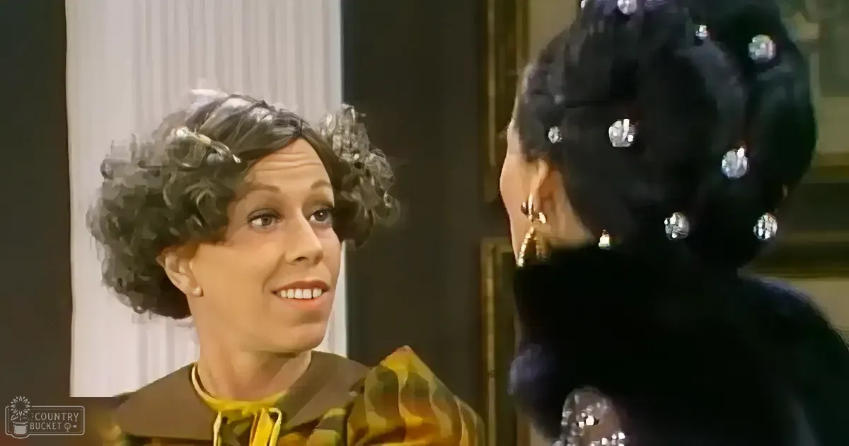 A woman with curly hair and a yellow and brown outfit smiles at another woman in a black dress with sparkling details.