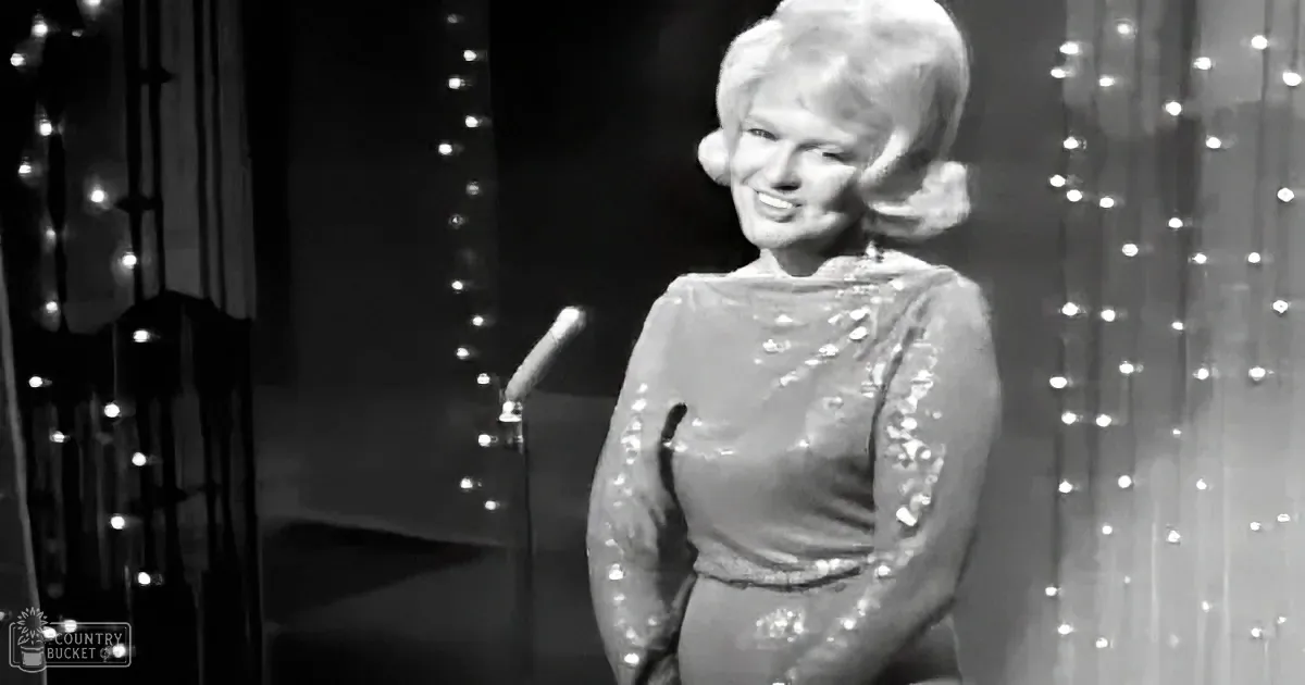 A woman in a sequined dress smiles on stage with twinkling lights in the background.