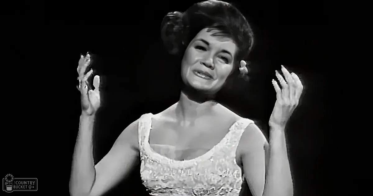 A woman in a white dress with lace details is smiling and clapping her hands.