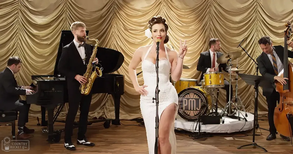 A woman in a white dress sings on stage with a band playing jazz music.