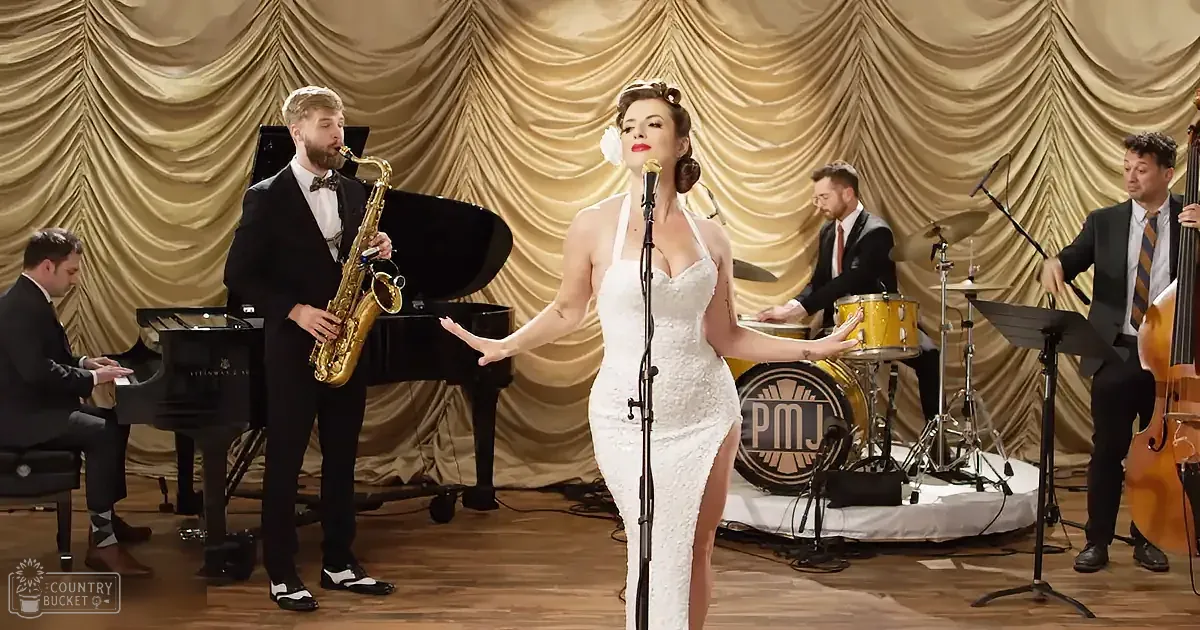 A woman in a white dress sings on stage with a band playing jazz music.
